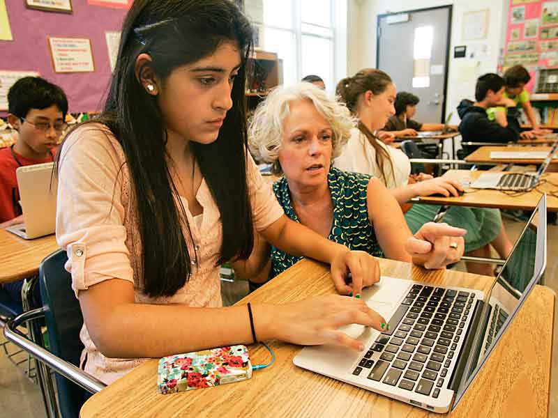 The author, Laura, crouches next to a young novelist working on a computer in a classroom filled with student writers.