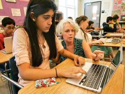 The author, Laura, crouches next to a young novelist working on a computer in a classroom filled with student writers.