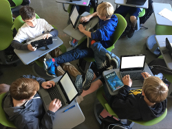 A group of young students sit at desks arranged in a circle, writing